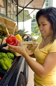 Teenage girl buying colored peppers at a farmers market.