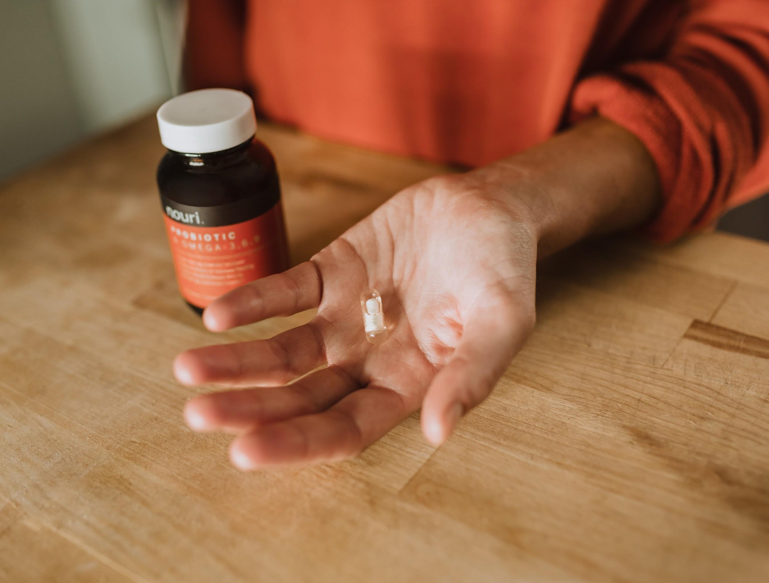 Woman holding probiotic capsule in her hand next to brand bottle over wooden counter.