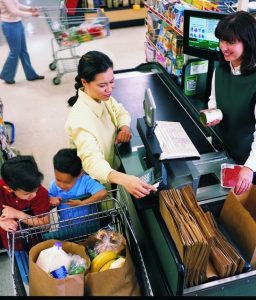 Mother with two young boys using SNAP benefits to buy groceries. Lady checking out the family is smiling as is the mother.