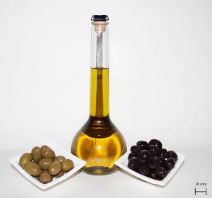 The center is a bottle of olive oil with a bowl of green olives on the left and black ones on the right.