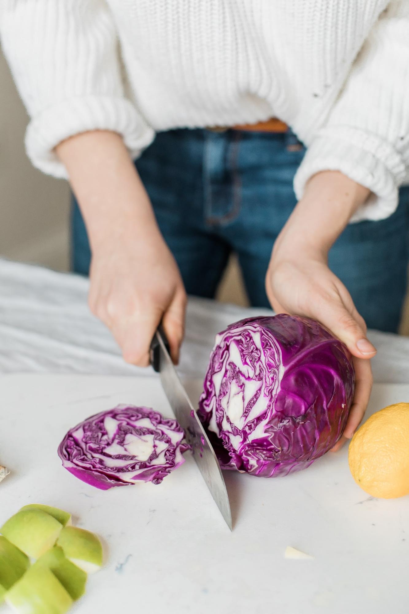 The image shows hands slice a large purple cabbage on a cutting board.