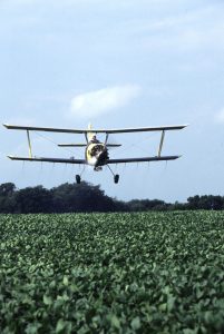Crop duster plane flying over a field to spray pesticides over the crops.