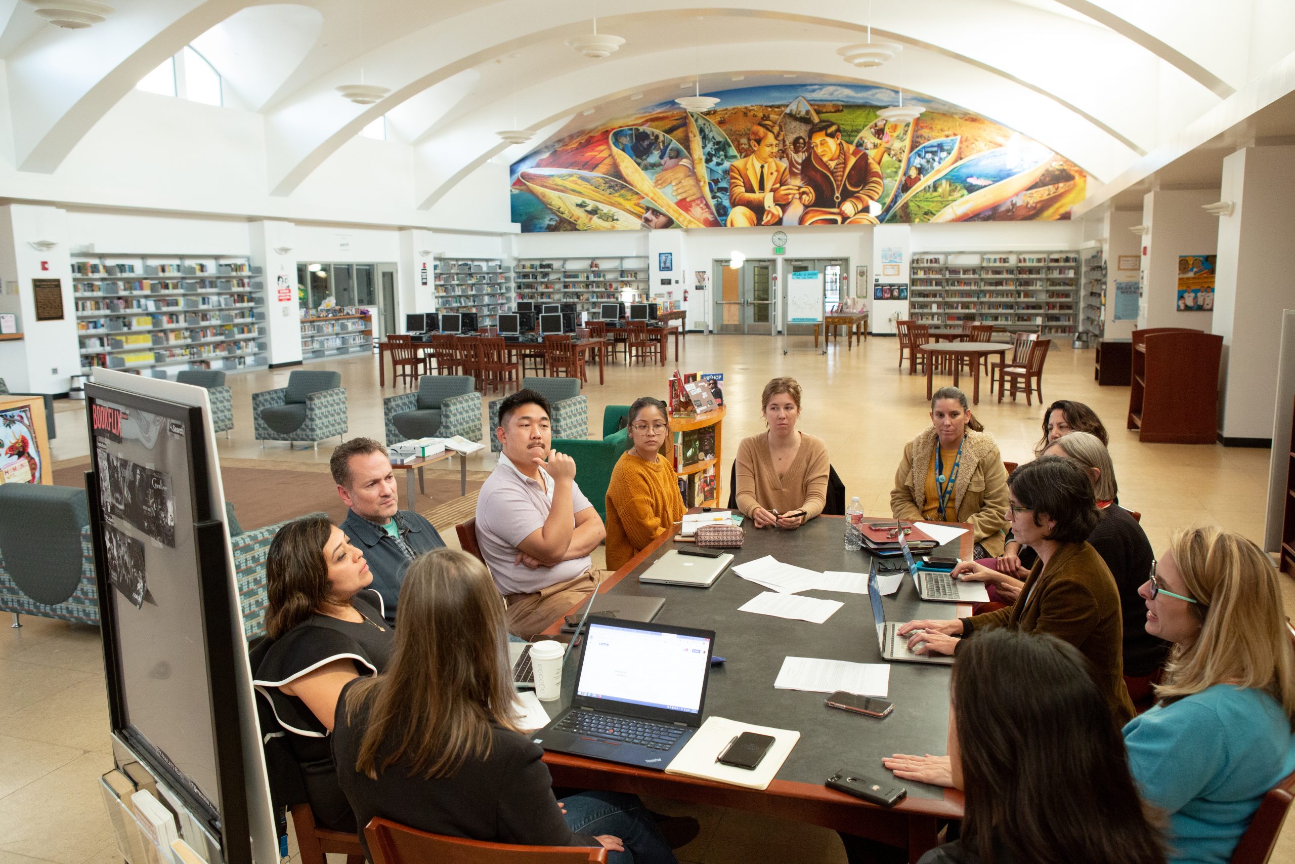 adults of various backgrounds seating around a table in a library